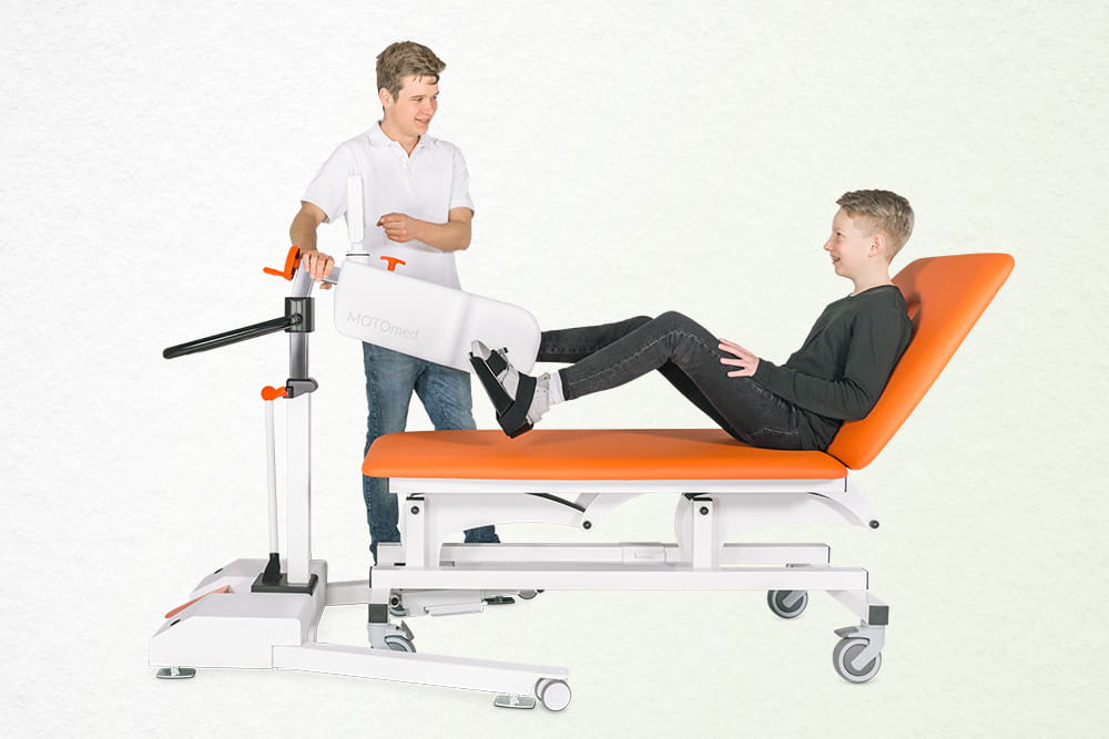 Ein Junge auf der Liege nutzt einen Bewegungstrainer.