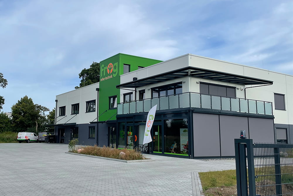 Außenansicht vom Neubau der FROG mit Blick auf die Front des Gebäudes. Im Vordergrund sieht man den neu gepflasterten Bereich und eine Bepflanzung.