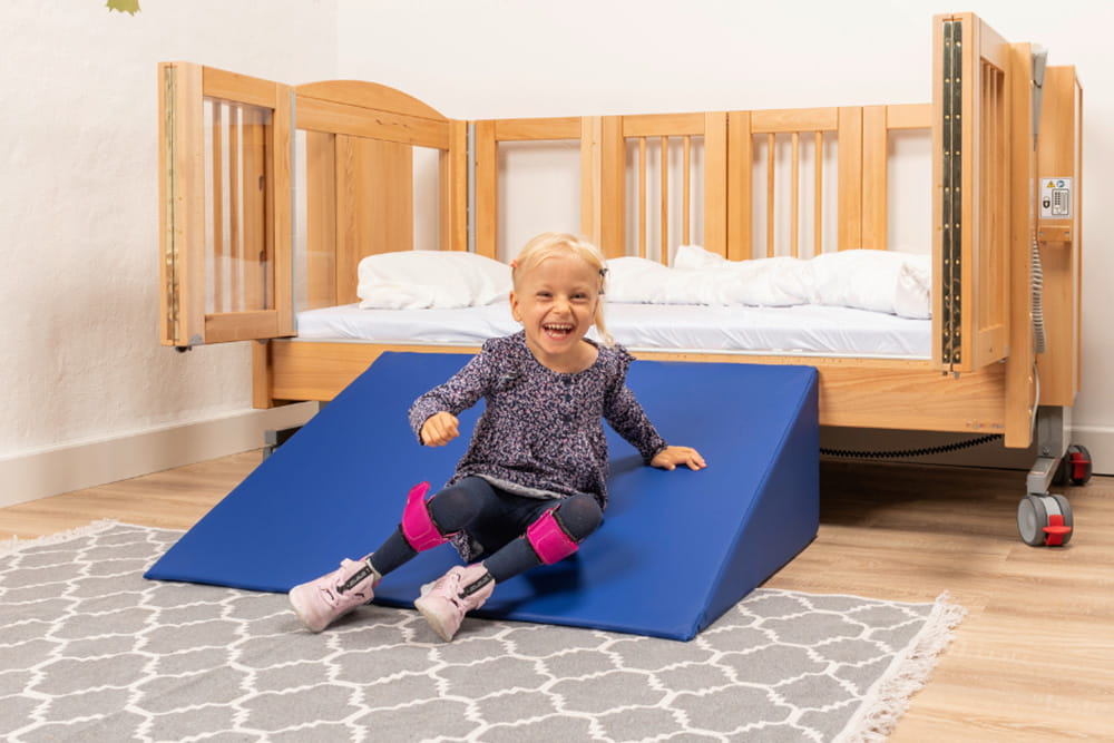 Ein kleines Mädchen rutscht auf der Rampe von ihrem Bett herunter.