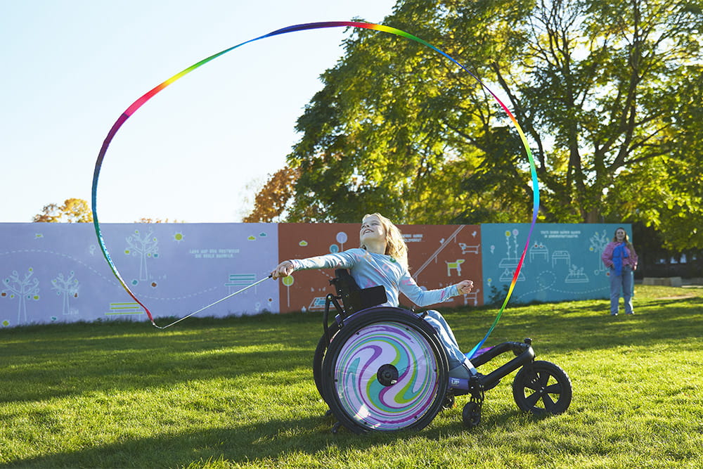 Ein Mädchen im Rollstuhlspielt mit Gymnastikband auf einer Wiese.