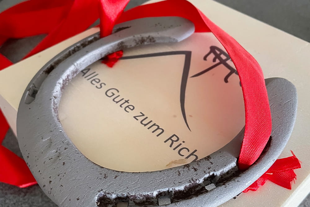 Ein Hufeisen an einem roten Band auf einem Schild, auf dem "Alles Gute zum Richtfest" steht.