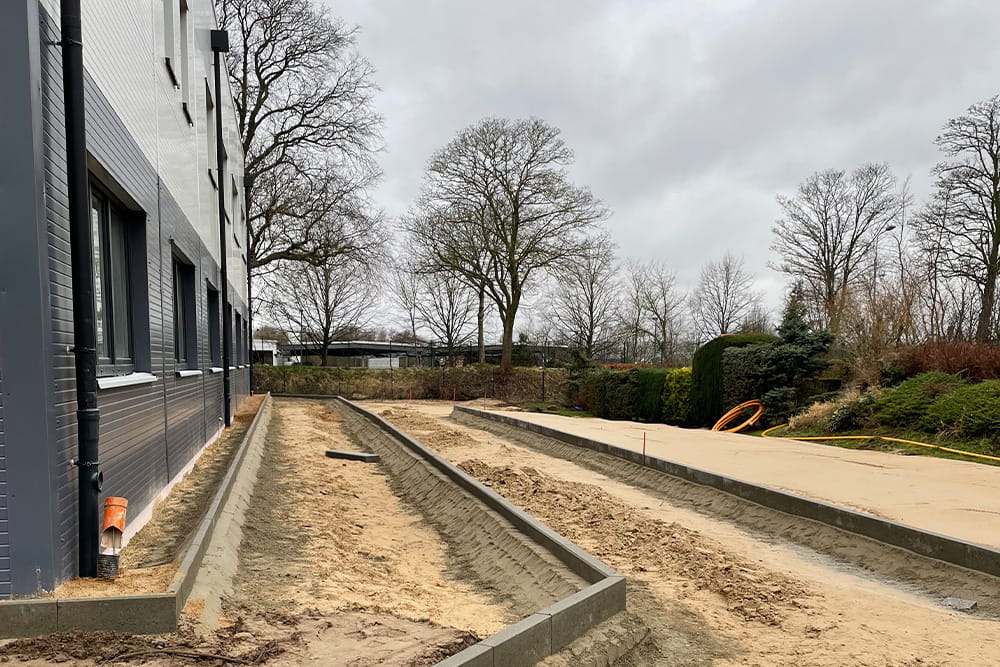 Außenansicht vom Neubau der FROG entland einer Wand. Man sieht viel Sand und die ersten Kantsteine für den Gehweg sind gesetzt.