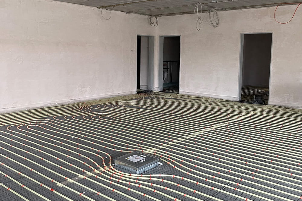 Ein Bild vom Bau das die Installation von sehr vielen schläuchen für die Bodenheizung zeigt.